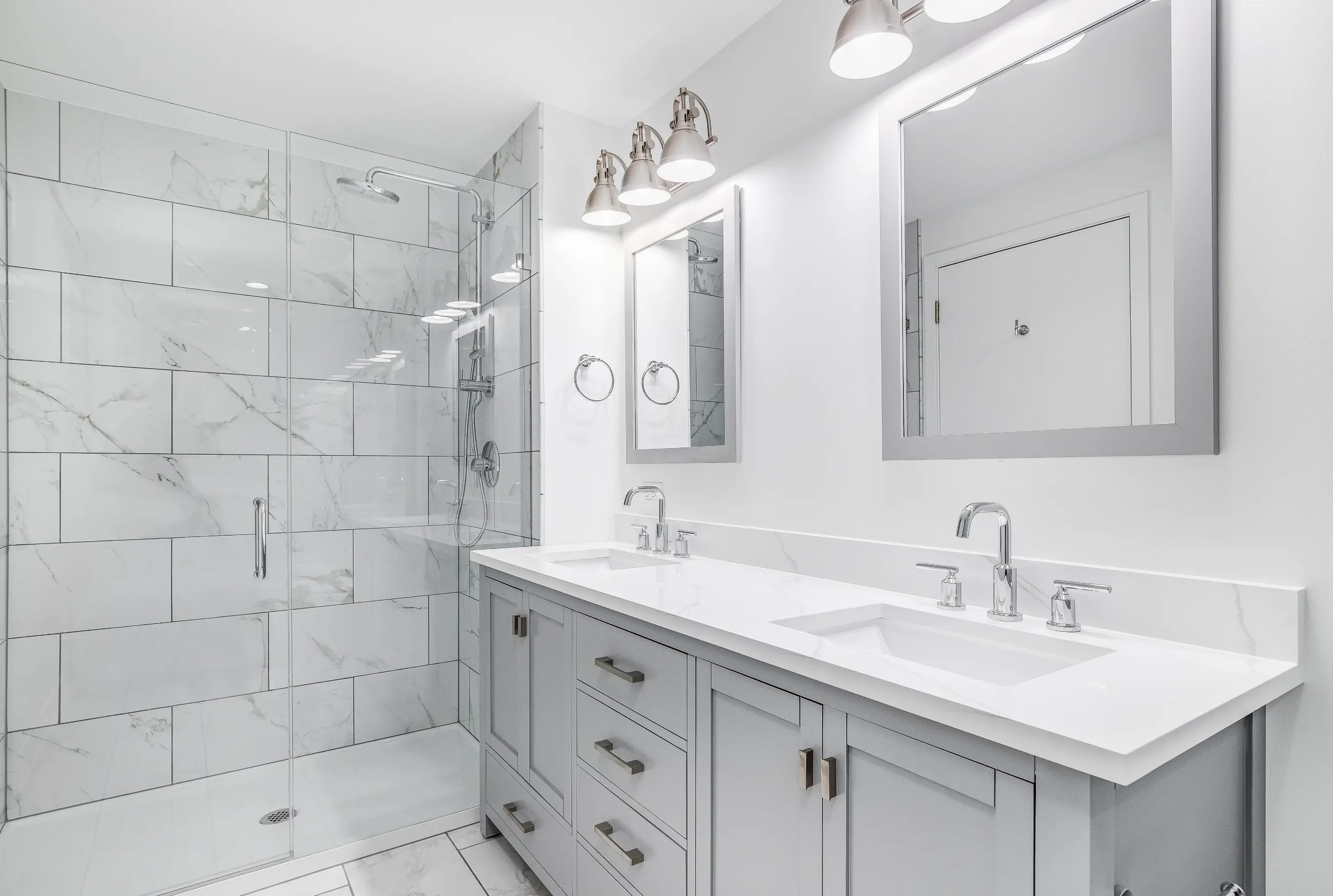 Modern bathroom remodel in Philadelphia featuring a double vanity with mirrors, glass-enclosed shower, and elegant tile work.