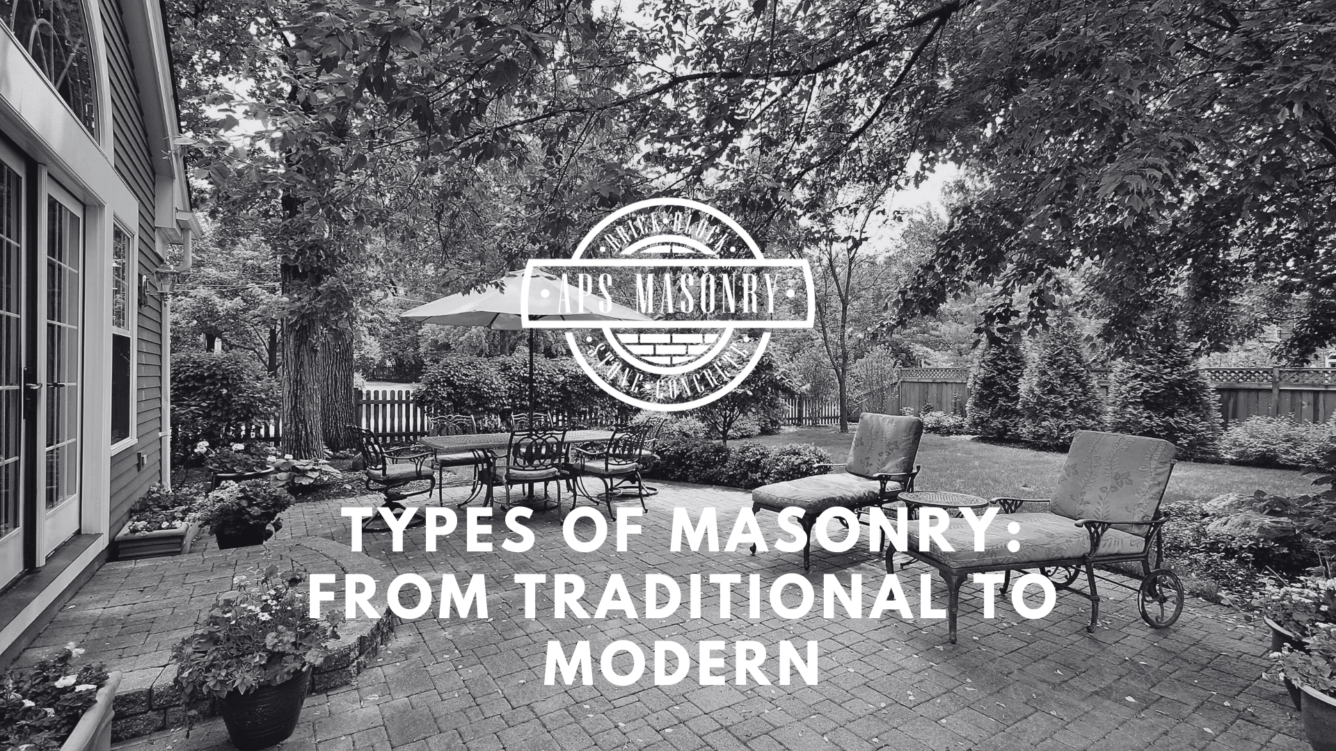 A black and white photograph of a serene backyard patio with a brick paved floor, surrounded by lush foliage and outdoor furniture. The APS Masonry logo is prominently displayed in the foreground, with the text 