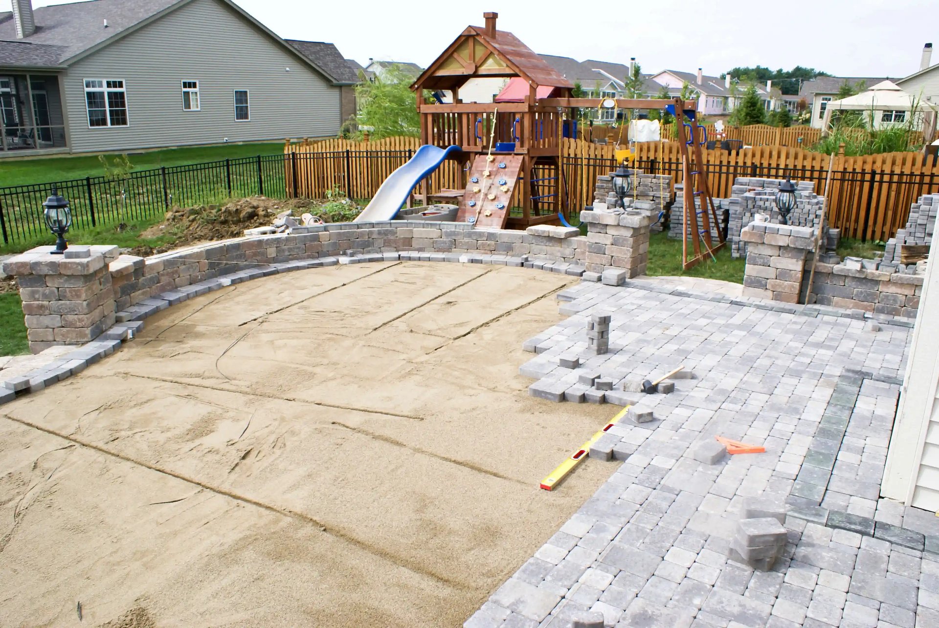 Backyard patio construction in progress by experienced masonry contractors in Montgomery County, PA, featuring a play area and partially completed stonework