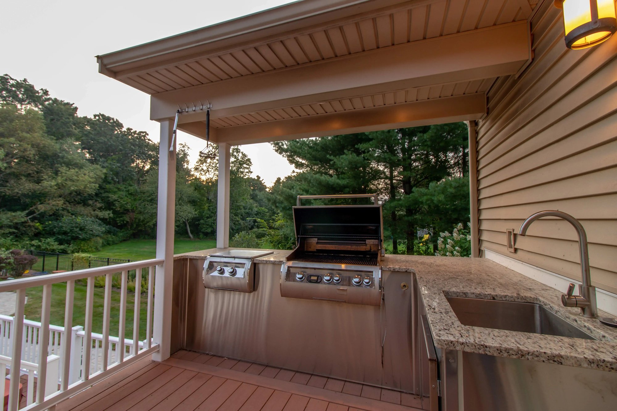 Outdoor covered grilling station with stainless steel appliances and granite countertops, overlooking a lush backyard