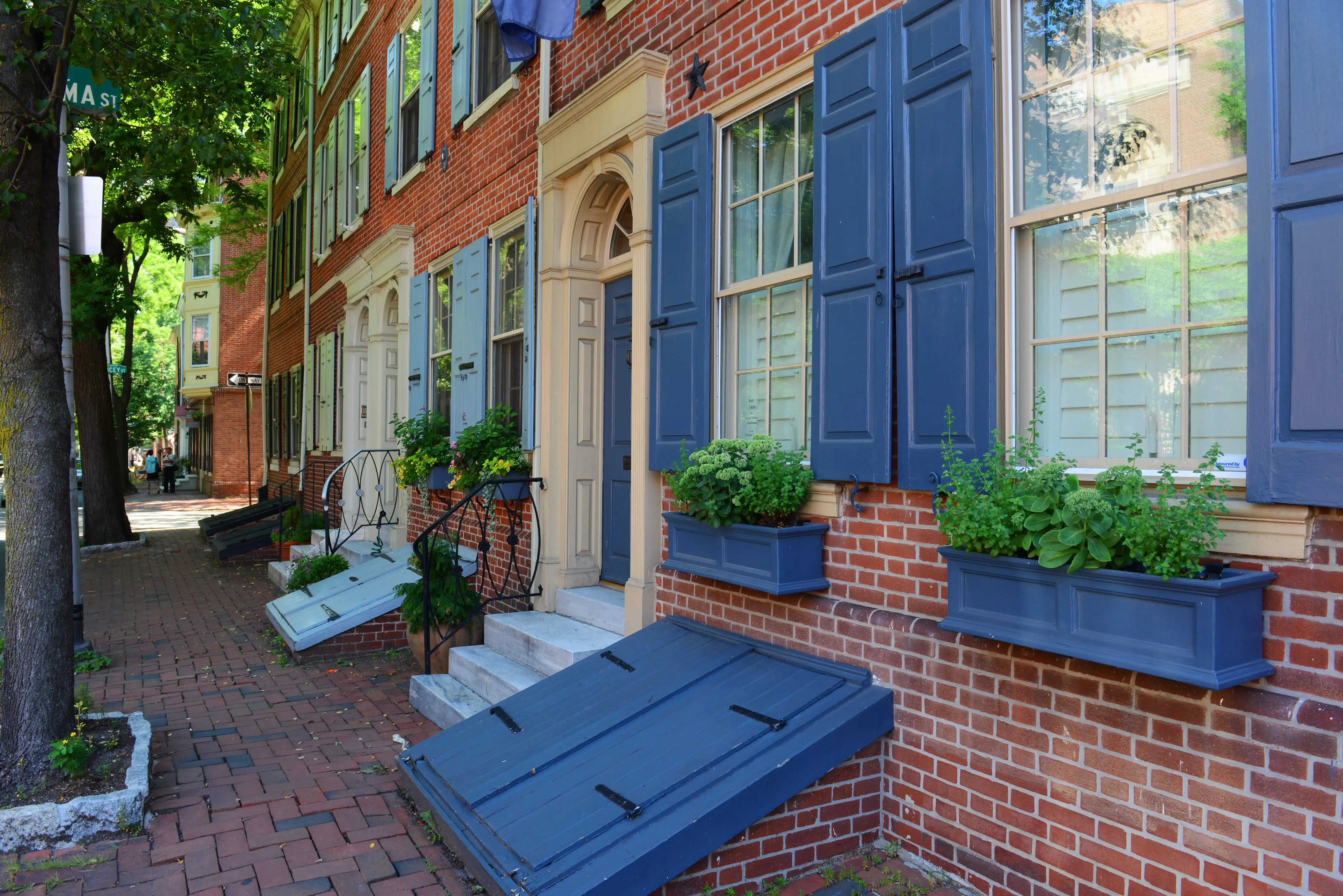 Beautifully renovated historical row homes in Philadelphia with blue shutters and window boxes filled with greenery