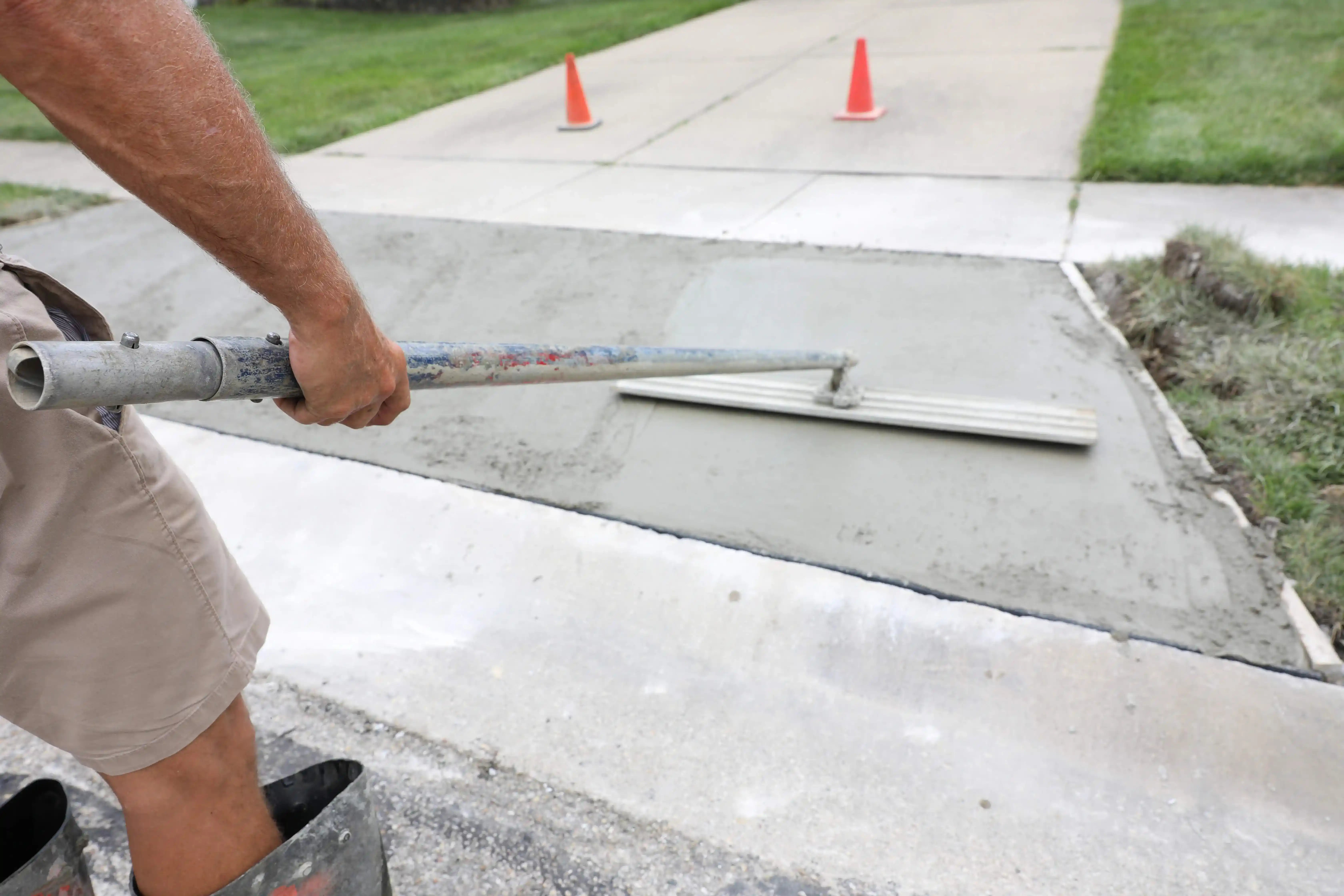 Worker using a bull float to smooth freshly poured concrete for patio repair.