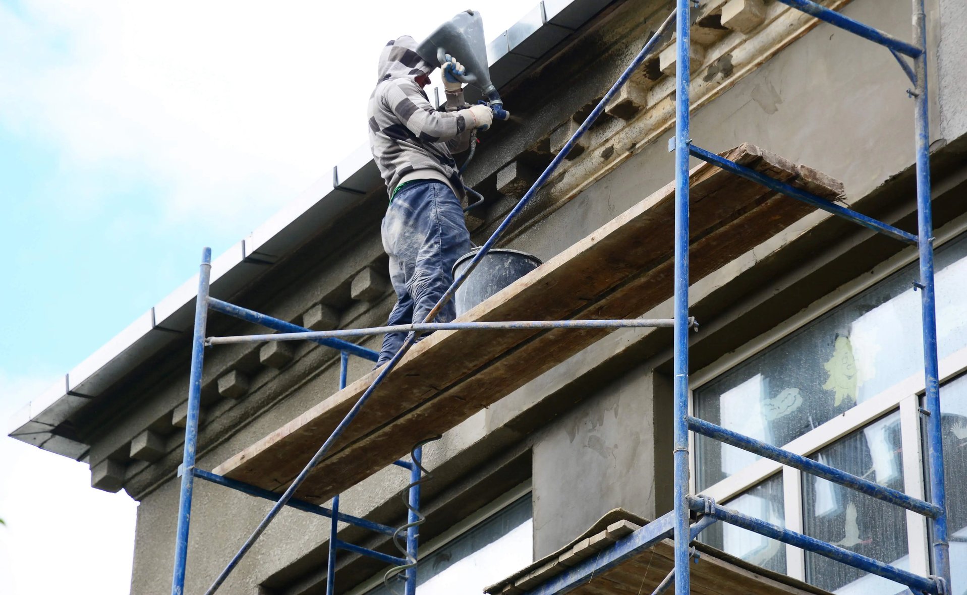Worker on scaffolding performing stucco remediation on a building facade in Philadelphia.