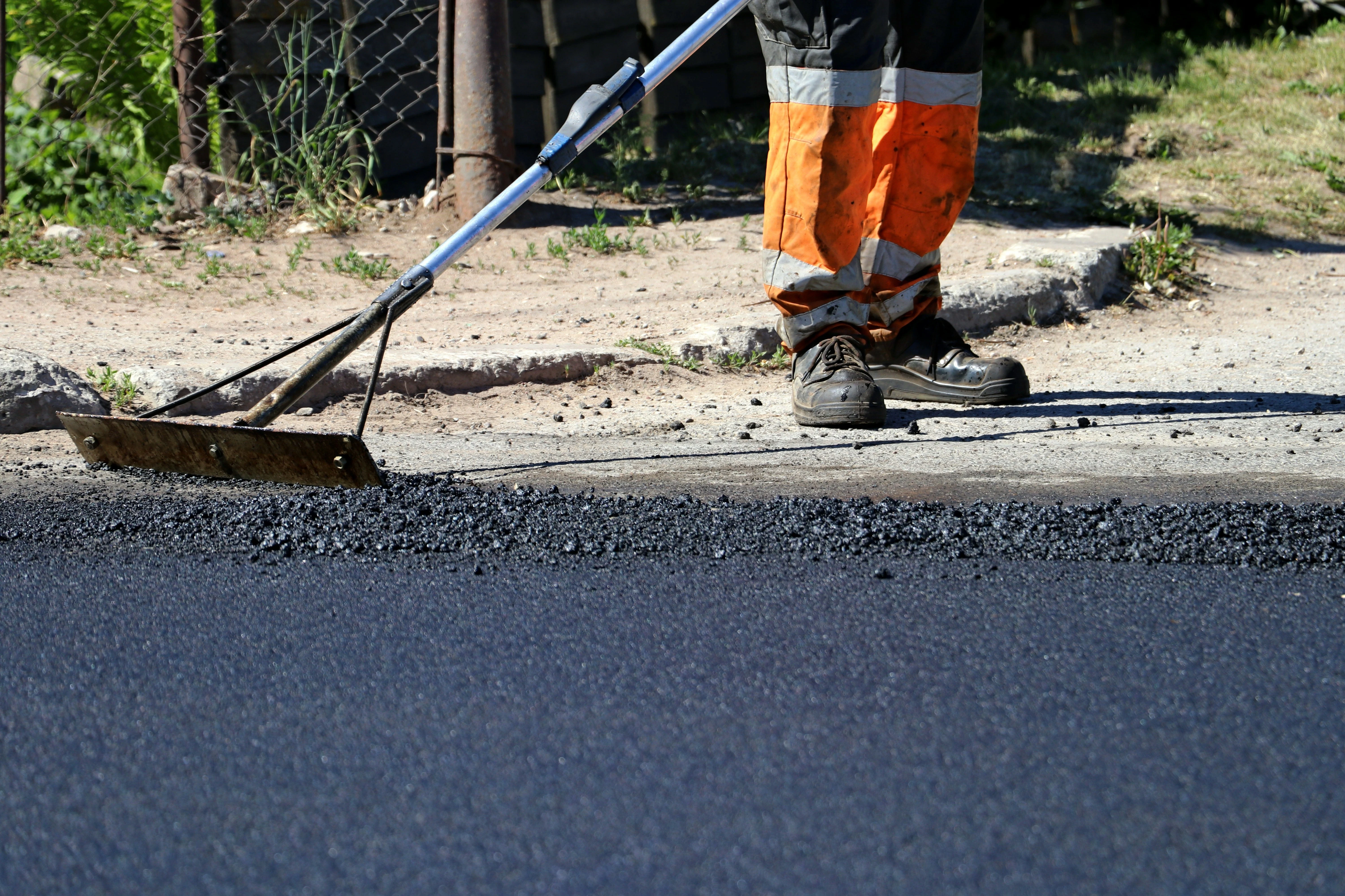 Worker in orange safety gear smoothing freshly laid asphalt during driveway repair.